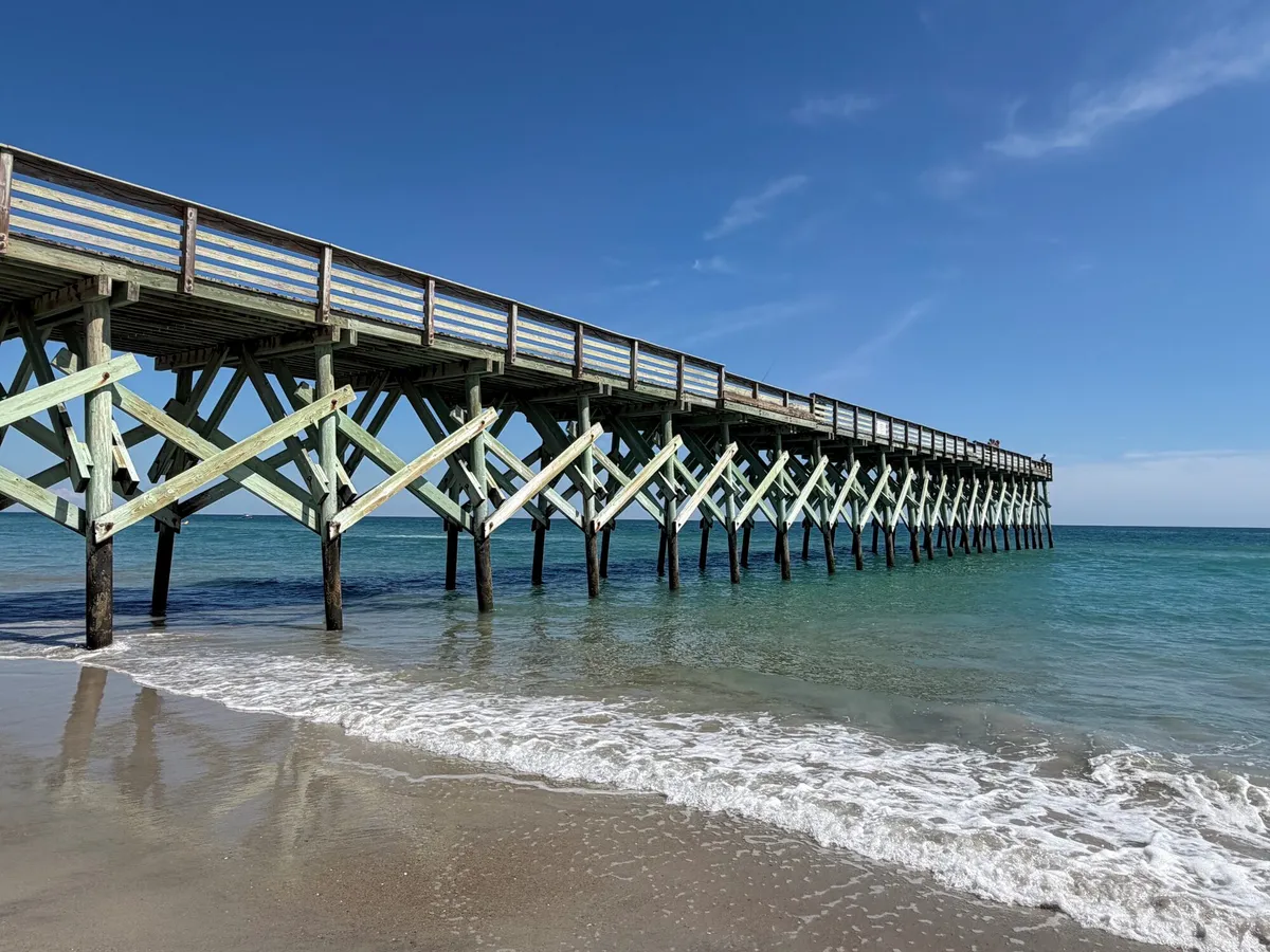 A timber fishing pier on braced piles running out from a beach into the ocean