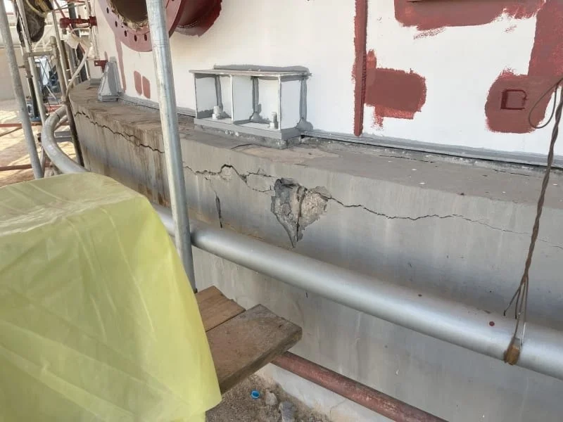 Cracked and spalled concrete foundation under a steel vessel, seen from scaffolding