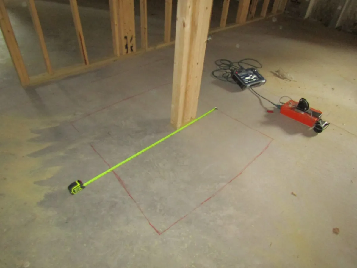 Test equipment and a tape measure on a marked concrete slab inside a framed house