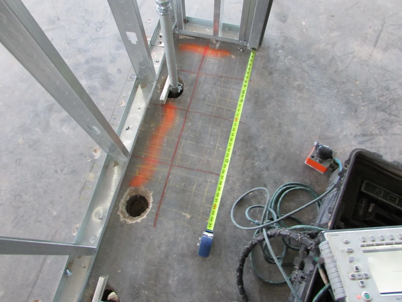 A slab marked out with paint and tape after a ground-penetrating radar scan, next to a core hole